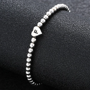 Macro shot of silver beaded elastic bracelet featuring a heart charm with letter F