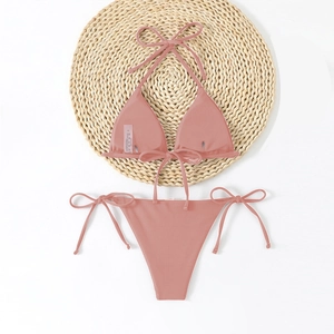 Detail of dusty pink ribbed bikini set with neck ties and side-tie bottoms on straw mat