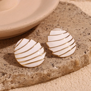 Detail of gold-plated spiral shell earrings with white enamel on a stone surface
