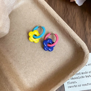 Macro shot of colorful asymmetrical daisy flower hoop earrings on a pulp tray