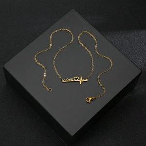 Minimalist gold LOVE heartbeat necklace on matte black jewelry box at 45-degree angle