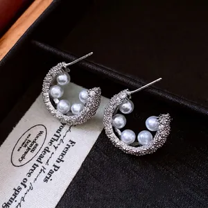 Elegant C-shaped earrings with pearls and rhinestones on a vintage jewelry box display