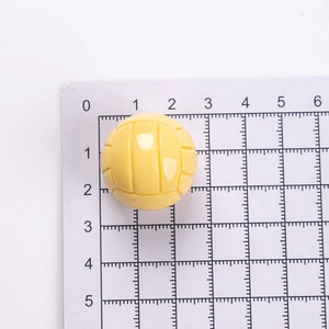 Vue macro d'un pendentif volleyball en résine jaune de 2,5 cm sur une règle graduée