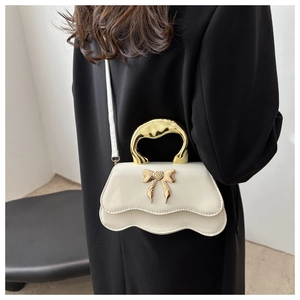Detail of cream mini crossbody bag with gold bow clasp and wavy metallic handle