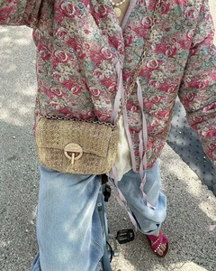 Detail showing khaki straw shoulder bag with metallic lock and chain strap on model