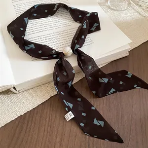 Vintage silk scarf necklace with geometric pattern and acrylic slide bead on a book