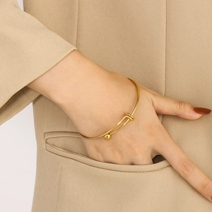 Close-up of golden minimalist retractable steel ball bracelet on model wrist with khaki suit
