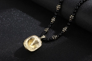 Detail of black beaded necklace with golden textured pendant and mantra charms