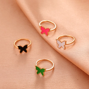 Detail view of four gold butterfly rings in red, black, white, and green on silk