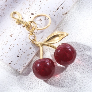Detail of red cherry keychain with gold leaves on a white stone background