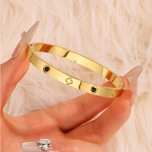 Detail of gold titanium steel clover bracelet with black zircon inlays on fur background
