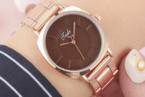 Gros plan d'une montre Tadi en métal or rose avec cadran marron portée au poignet femme