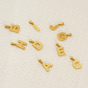 Elegant gold stainless steel alphabet pendants A-J on white textured fabric background