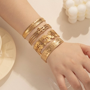 Set of four gold stainless steel cuff bracelets with feather and leaf designs on wrist