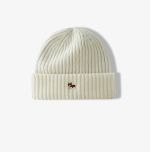 Close-up of cream knitted beanie featuring soft wool texture and small dog embroidery detail