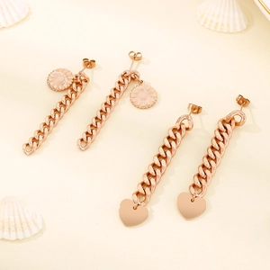 Detailed view of rose gold Cuban link earrings with sunflower and heart charms on white shells