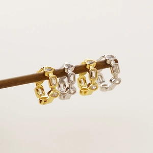 Detail van zilveren en gouden geometrische oorringen met hartvormige zirkoonstenen