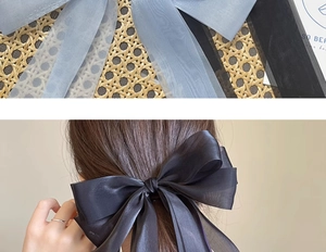 Detailed view of oversized ribbon bow hair clips in black and blue on a woven texture