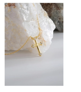 Detail of gold cross necklace with zircon stones on a white stone background