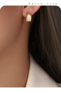 Detail of elegant crescent gold hoop earrings with white enamel inlay worn by model