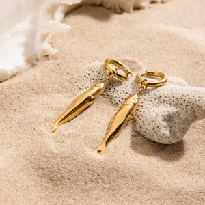 Detail of gold fish-shaped earrings on a sandy beach background with white coral décor