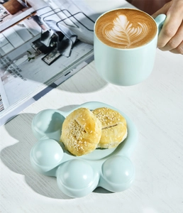 Close-up of ceramic cat paw plate and blue mug with coffee on white wood surface