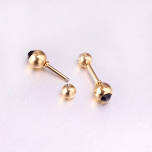 Detail of gold screw-back ball earrings with black cone inlay on metallic surface