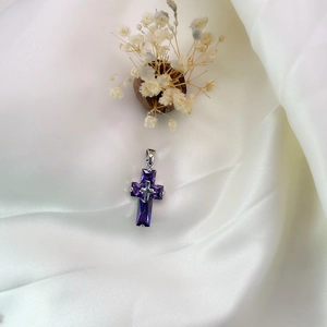 Detail of silver cross pendant featuring purple gemstones on elegant white silk