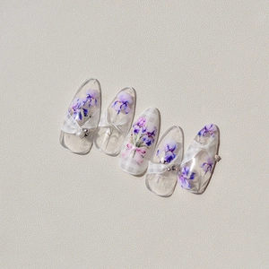 Detail of long pointed press-on nails with purple floral patterns and pearl accents