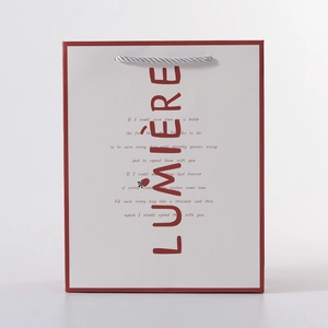 Detail of cream gift bag with red edges, silver rope handles and LUMIÈRE text