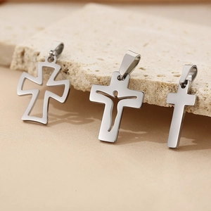 Three minimalist silver stainless steel cross pendants displayed on a textured stone