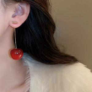 Close-up of elegant red cherry earrings with gold stems worn by a model in soft light