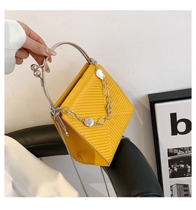 Detail of yellow geometric handbag with silver ring handle and chain on leather chair