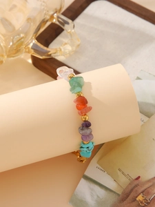 Detail of bohemian gold bead bracelet with colorful irregular stones on beige display stand