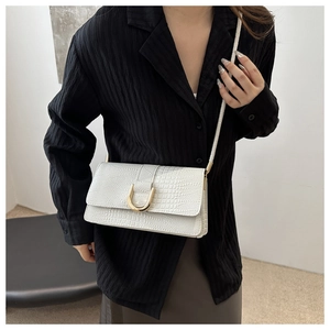 Détail d'un sac bandoulière blanc à motif crocodile avec boucle dorée en forme de U
