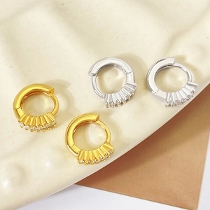 Macro view of gold and silver hoop earrings with clear zircon stones on a textured backdrop