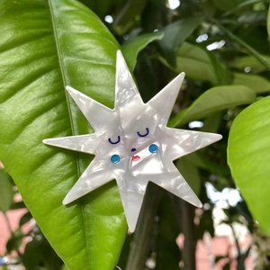 Macro detail of star-shaped acetate hair clip with cute face on green leaves