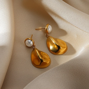 Detail of gold water drop pearl earrings displayed on elegant champagne silk fabric