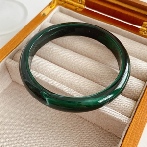Macro detail of polished dark green jade bangle in a premium wooden jewelry storage box