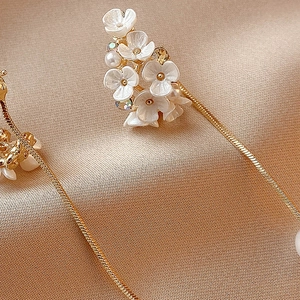 Dettaglio di nappine a fiori bianchi con strass e perle su seta color champagne lucida