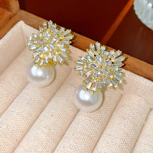 Close-up of gold flower earrings with crystals and pearl drops on beige jewelry cushion