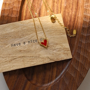 Elegant gold titanium steel necklace with a red heart pendant on a wooden tray display