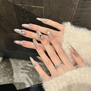 Vue détaillée d'ongles amandes dégradé champagne avec strass et perles sur les mains