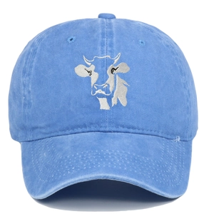 Detailed close-up of white cow embroidery on a blue washed cotton baseball cap