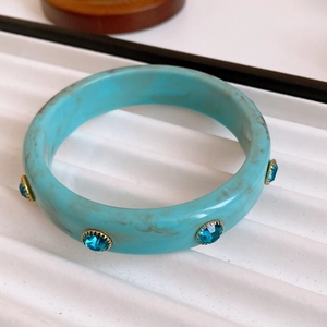 Macro detail of gold-plated bangle featuring turquoise marble resin and blue crystal