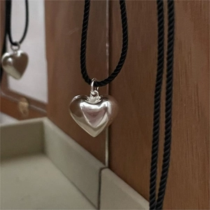 Macro shot of polished silver heart pendant on a black woven cord with wooden background