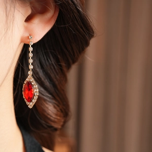 Close-up of model wearing gold drop earrings with red oval gemstone and crystals