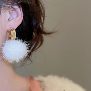 Close-up of white plush pom-pom earrings with gold textured metal hoops on model