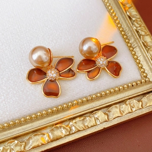 Détail de boucles d'oreilles fleurs ambrées avec bord doré et perle élégante