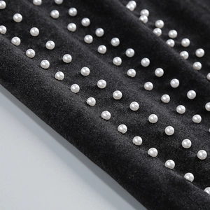 Détail de perles blanches sur tissu noir montrant la broderie élégante et la texture